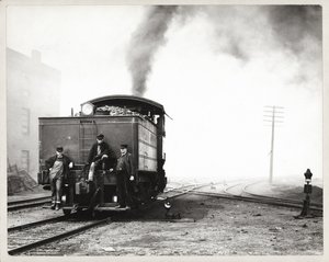 Drie mannen op de achterkant van een rangeerlocomotief in een onbekende spoorwegwerf